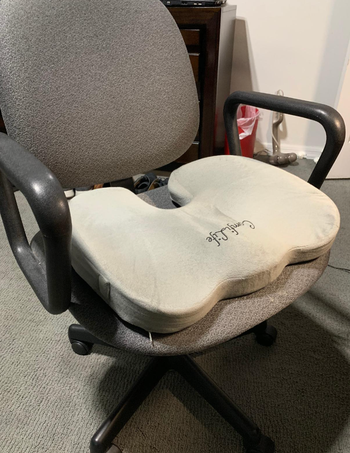 A gray pillow resting on the seat of an office chair.