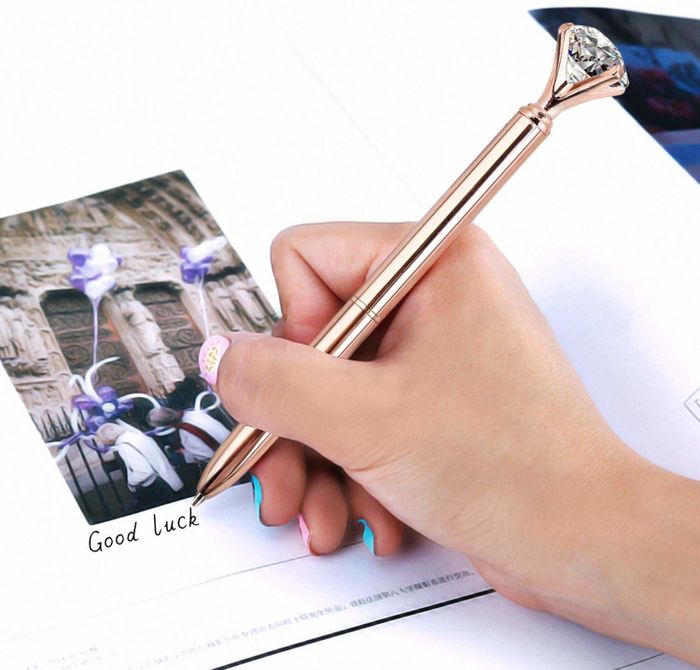 someone writing with a metallic pen topped with a large faux diamond
