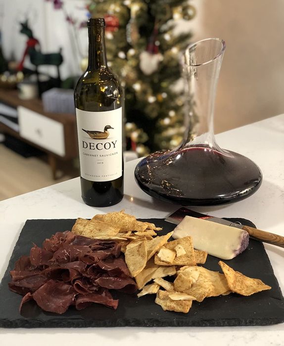 A reviewer’s photo featuring a glass decanter placed beside a platter of cheese and meats.
