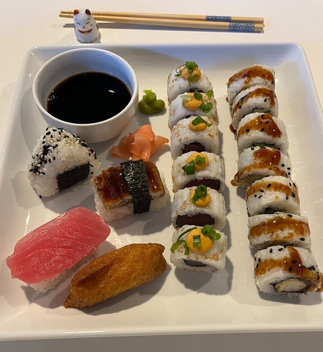 A beautifully plated assortment of sushi served with soy sauce, ginger, and wasabi. In the background, chopsticks and a small cat figurine are visible.