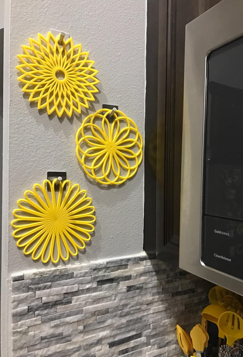 Three bright yellow flower-shaped trivet mats gracefully hung on a wall.