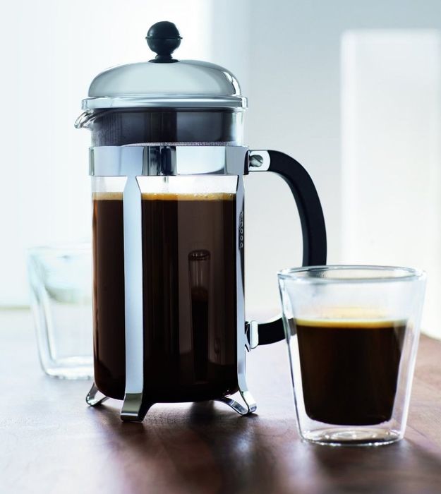 The French press, sitting next to a freshly brewed cup of coffee, ready to be enjoyed.