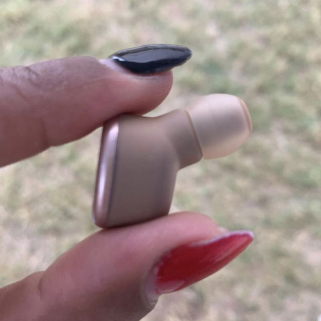 A reviewer holding up an earbud to showcase its compact size