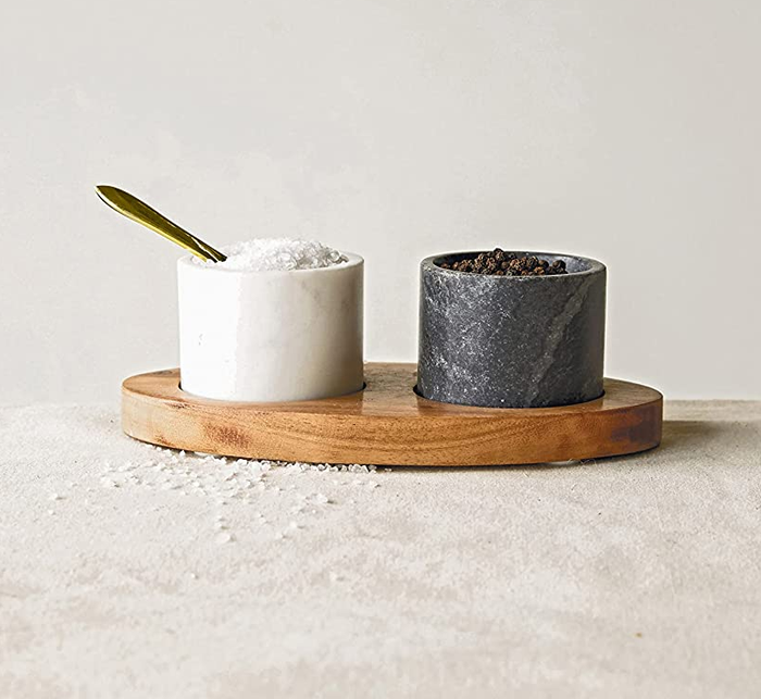A black cup and a white cup resting on a wooden tray, with a spoon placed inside the white cup