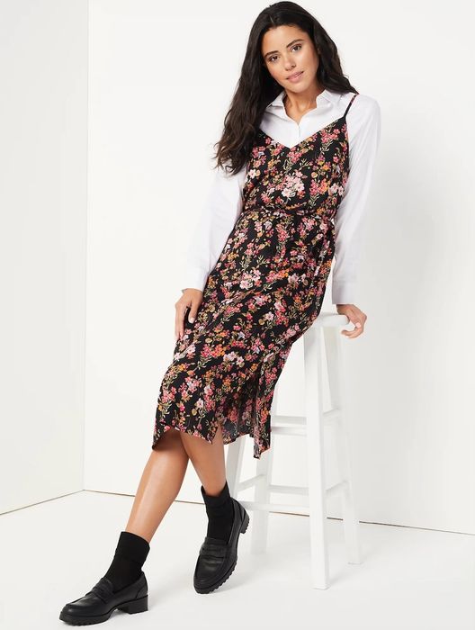 Model styling a black, white, yellow, and pink floral slip dress worn over a white button-down shirt, paired with black shoes and socks.