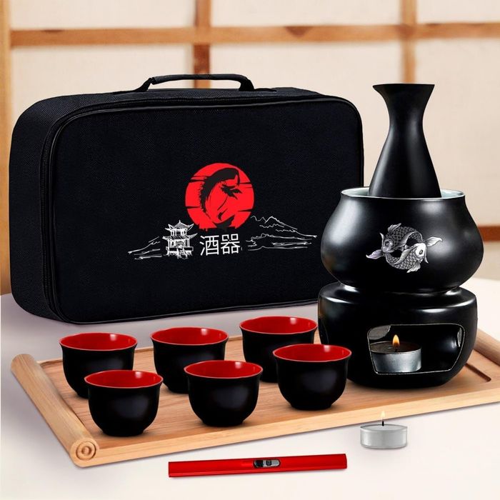 A Japanese sake set featuring black cups, a warmer, and a carrying case embroidered with a red sun and dragon motif. The set includes a candle and a silver warmer element.