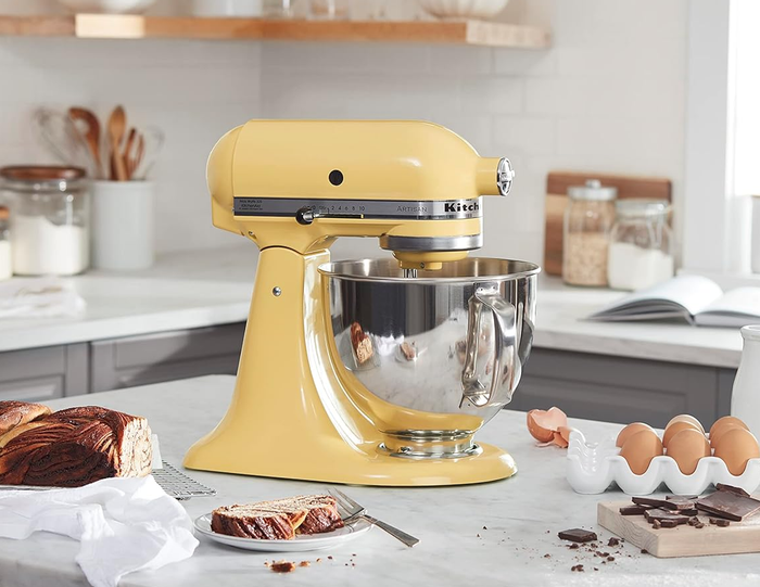 A yellow KitchenAid stand mixer placed on a kitchen counter with eggs, milk, and bread, evoking the essence of a cozy baking scene.