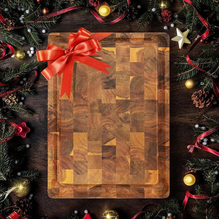 A decorative wooden cutting board adorned with a red bow, surrounded by festive holiday greenery and ornaments, making it the perfect gift for cooking enthusiasts.