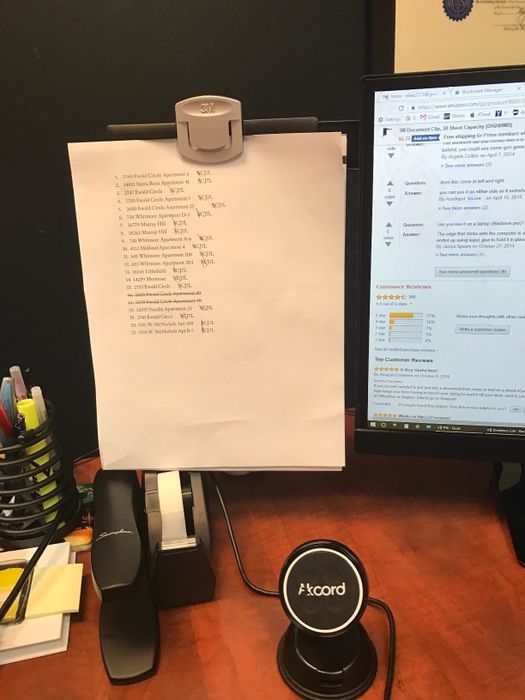 A reviewer's photo showing a clip extending from the side of a monitor, holding a document in place.