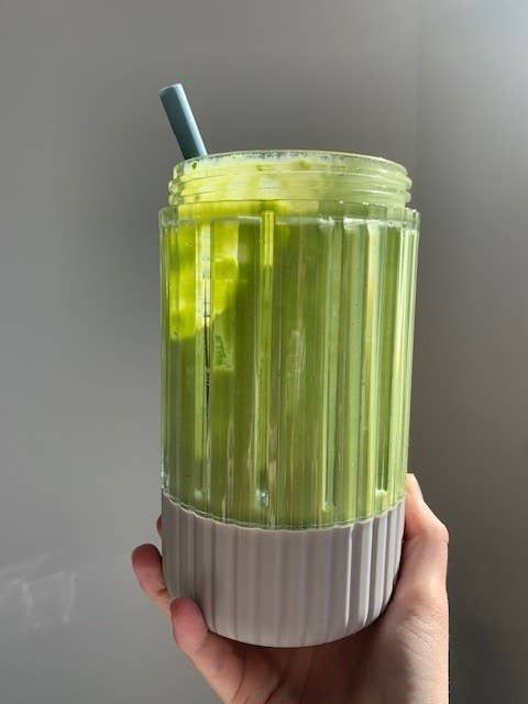 A transparent cup with vertical ridges, filled with a green smoothie and topped with a straw, perfect for shopping or lifestyle content.