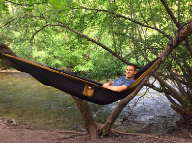 A person lounging in a hammock beside a serene river.
