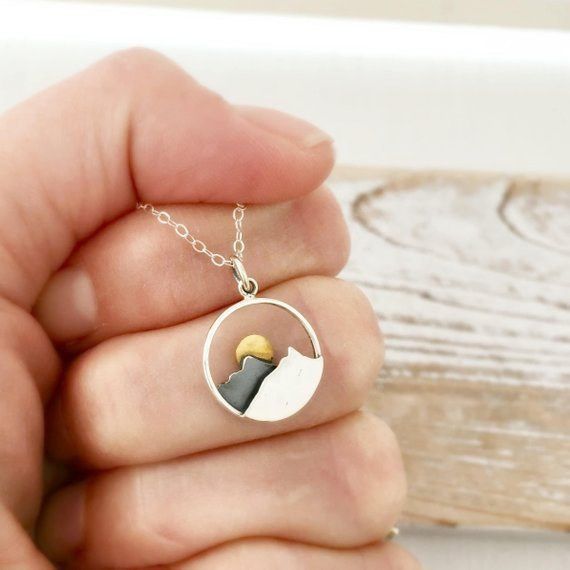 A hand holding a necklace with a pendant featuring a mountain range and a glowing sun.