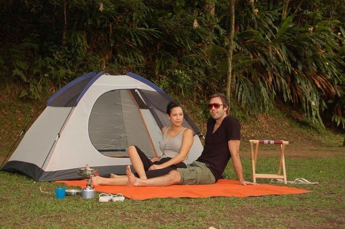 A group of people enjoying the outdoors, sitting comfortably on the mat beside their camping tent.