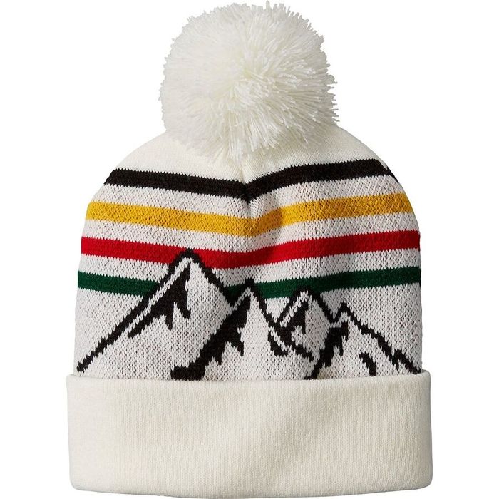 A white beanie topped with a white pom, featuring Pendleton stripes and a design of mountain ranges.