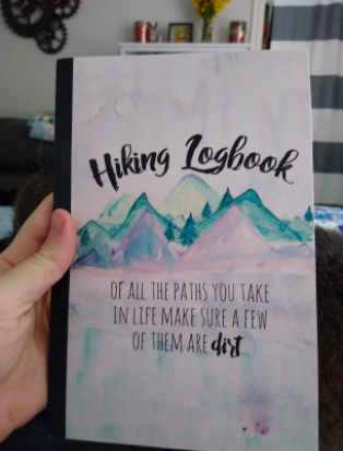 A hand clutching the logbook, featuring a watercolor mountain design on its cover.