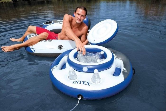 A person lounging on a raft, enjoying a refreshing drink from a floating cooler on the water.