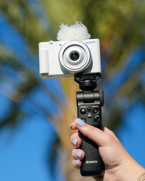 A person holding the camera mounted on a tripod, against a white background.