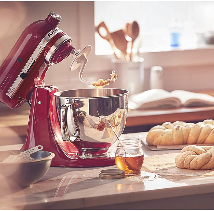 The red stand mixer with its head tilted back and the dough hook attachment in place, sitting next to some shaped loaves of dough.