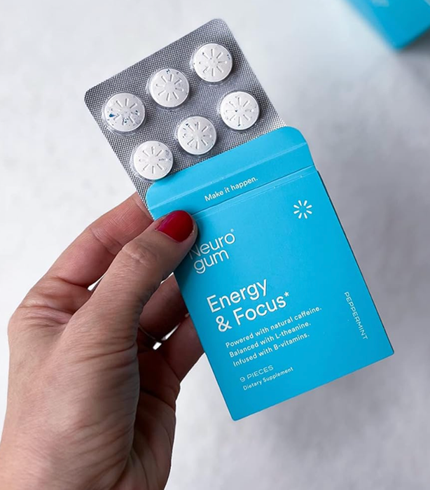 A reviewer holding a small blue box containing a pack of white round gum