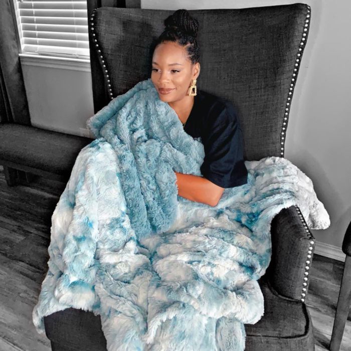 A reviewer snuggled up in the cozy arctic blue fleece-lined throw blanket.