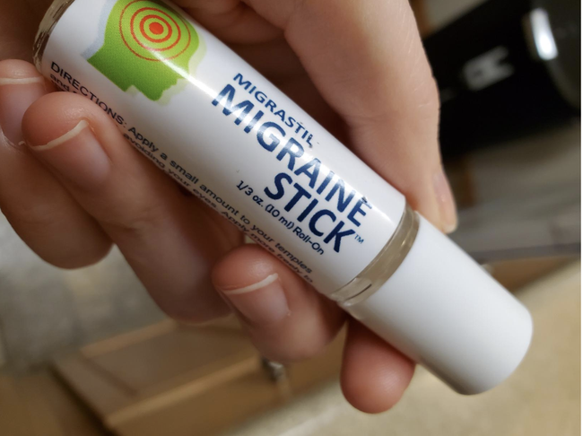 A reviewer holding a small, lip balm-sized tube of migraine relief roll-on stick.