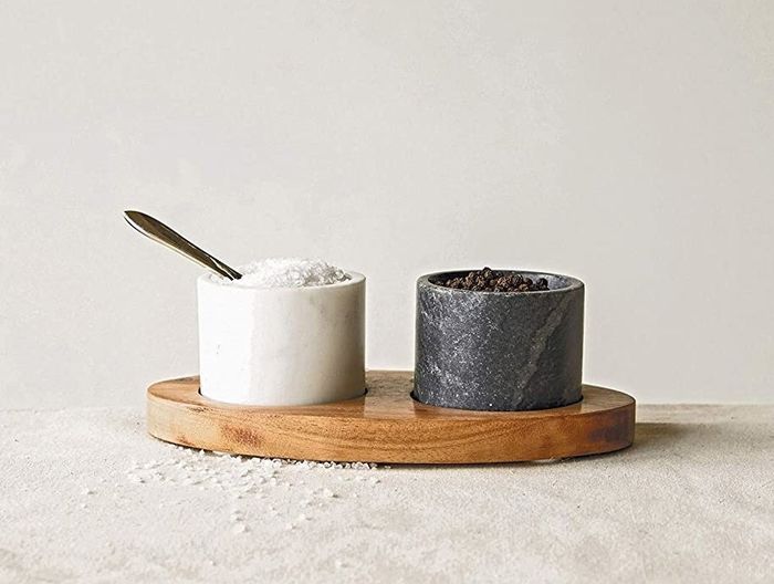 A black and white marble bowl sitting on a wooden tray, with salt in one and pepper in the other.