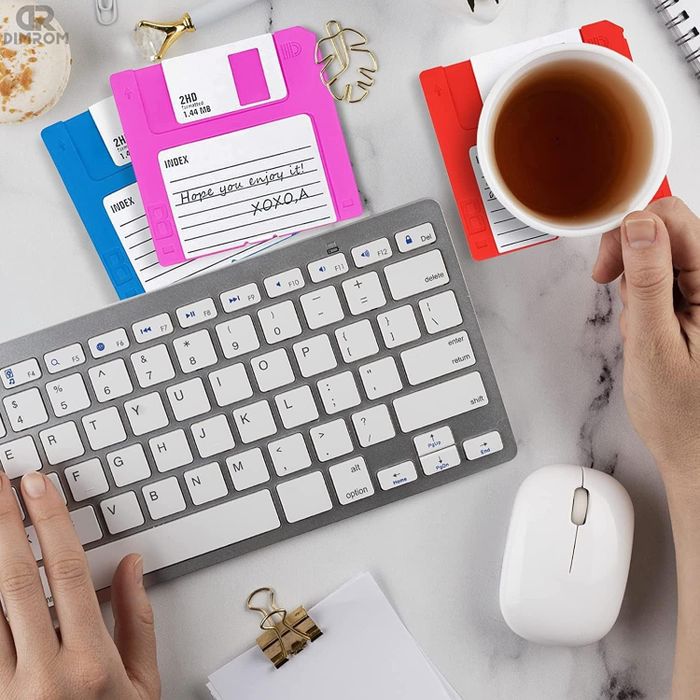 Three coasters designed like neon floppy disks in shades of pink, orange, and blue with playful messages written on them