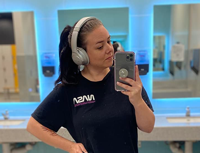 A reviewer in a gym locker room wearing the silver pair of headphones