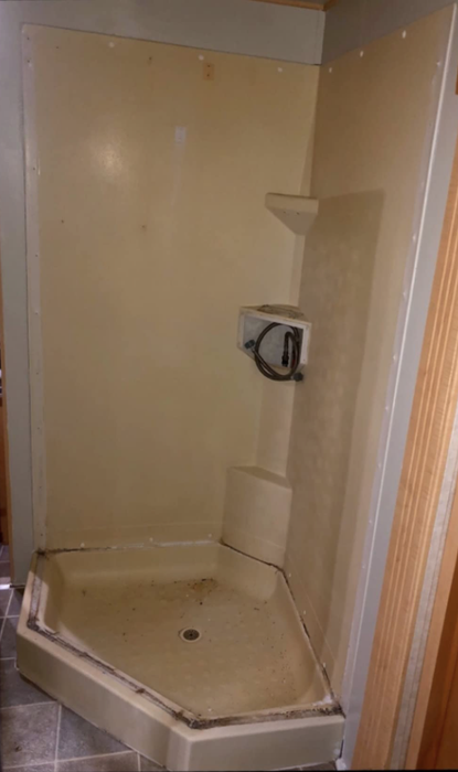 A shower surround and floor that appear discolored, yellowed, and covered in mold, looking far from fresh.