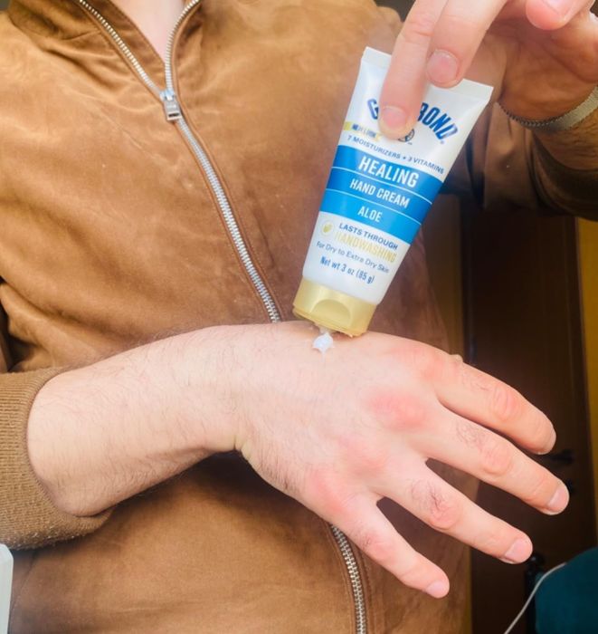 A person applying aloe-infused healing hand cream from a tube onto their hand