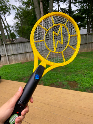 A reviewer holding a tennis-style swatter in a backyard.
