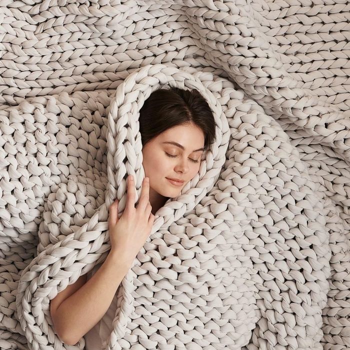 A model snuggled up in a soft ivory knit weighted blanket