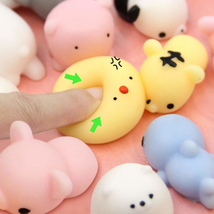 A finger pressing down on a yellow squishy toy shaped like a chick.