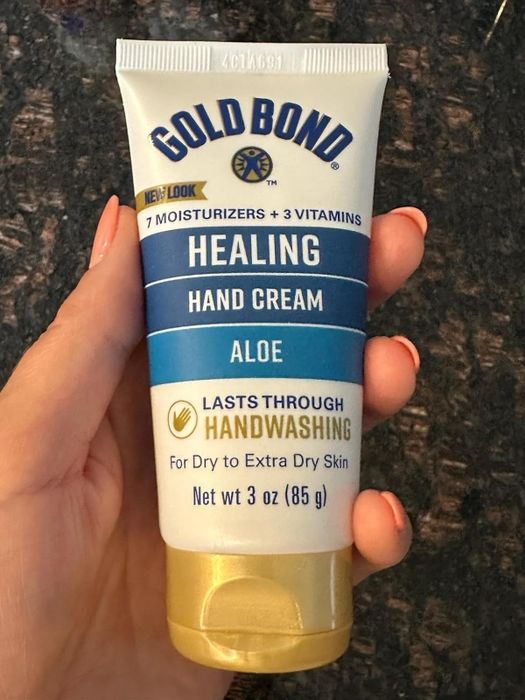 A person holding a tube of Gold Bond Healing Hand Cream with aloe, designed for dry to extra dry skin and resistant to handwashing