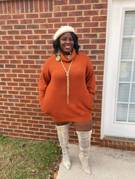 A reviewer models the orange dress, pairing it with a statement necklace and over-the-knee boots for an added touch of flair.