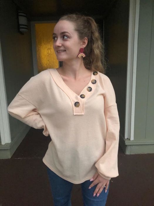 A reviewer shows off an apricot-colored shirt, demonstrating its stylish appeal.