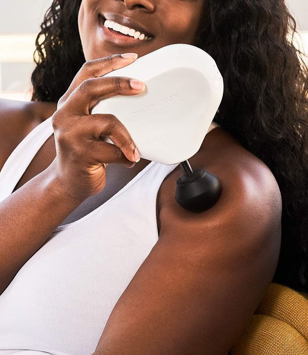 A person applying the mini Theragun to their shoulder for a soothing massage.