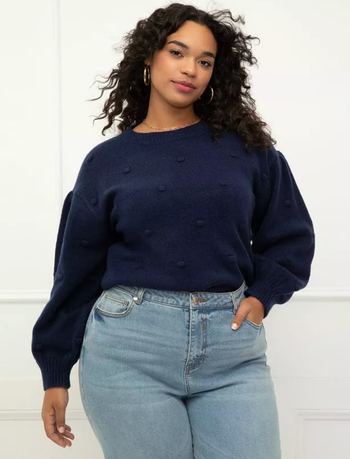 A model is showcasing a navy-colored bobble sweater paired with jeans.