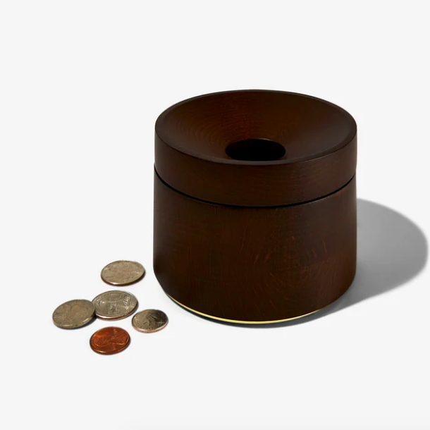 A cylindrical bowl with a lid and an open top, with a few coins placed beside it