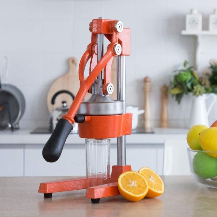 A hand press juicer with a cup underneath and orange halves beside it
