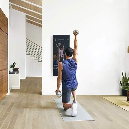 A model lifting weights with an instructor displayed on the mirror's screen.