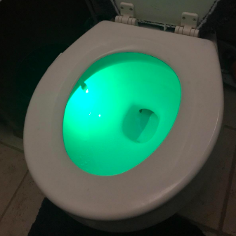Another reviewer image of a toilet seat glowing a vibrant green in a well-lit room.