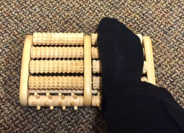 A reviewer demonstrating how to use the massage roller by placing their foot on it.