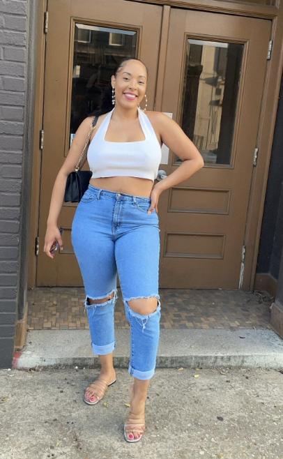 The reviewer is dressed in a white top, ripped blue jeans, and sandals.
