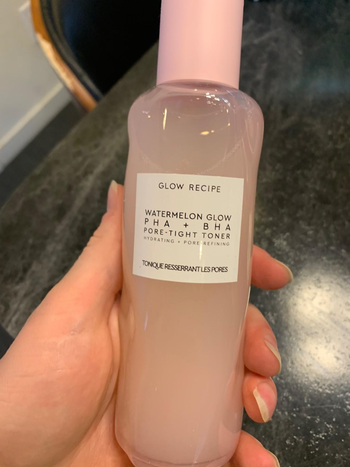 A reviewer holding a pink product bottle.