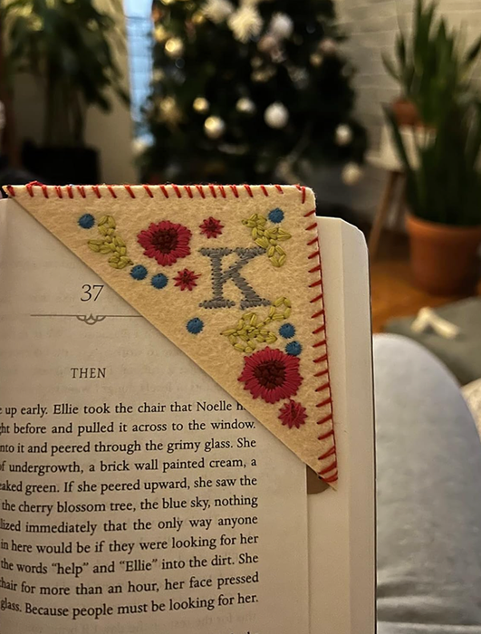 A book with a felt corner page bookmark, featuring an embroidered 'K' and floral designs.