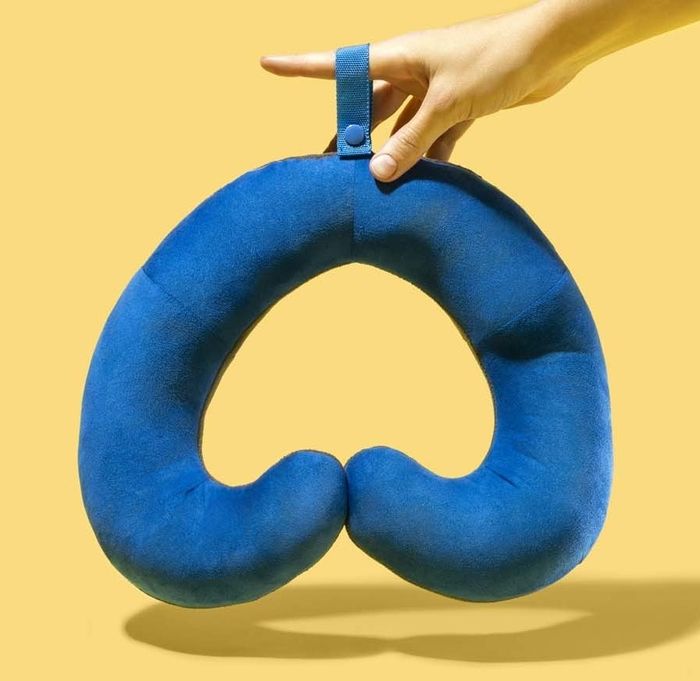 A hand holding a blue travel pillow with soft, curled ends designed to wrap around the neck.
