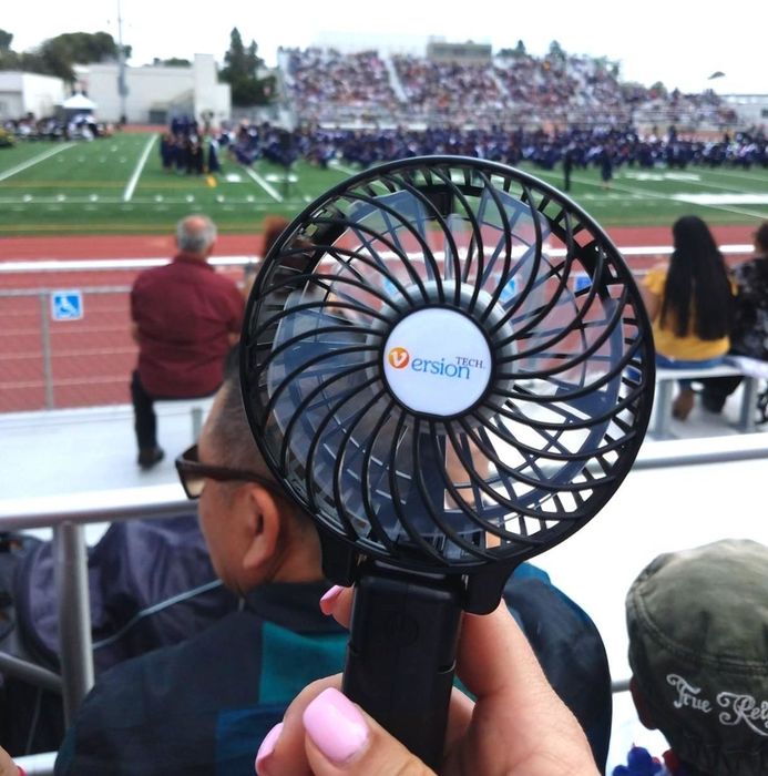 A reviewer holding up a black personal fan outdoors.