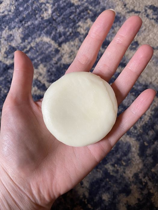A round conditioner bar resting in the palm of a hand.