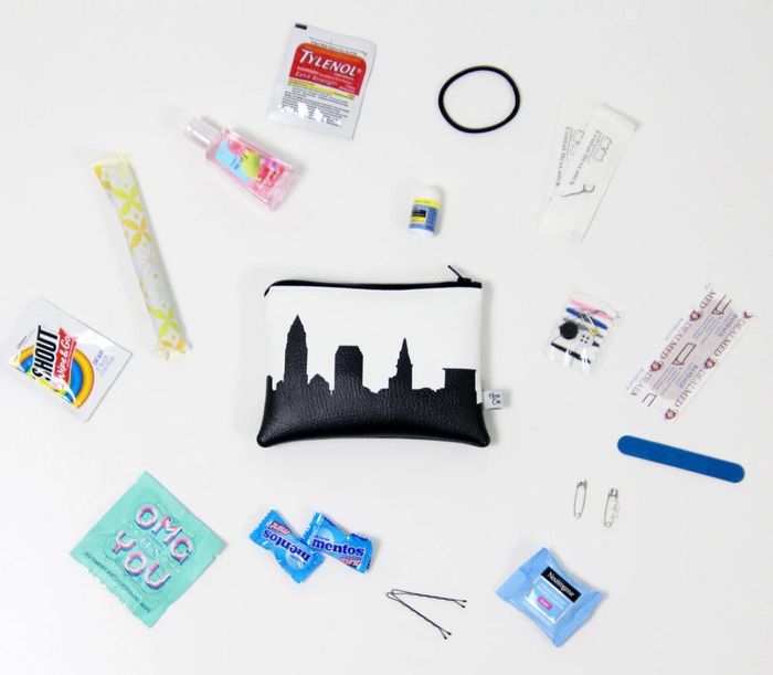 A small white faux leather pouch with a black city skyline print, filled with a variety of travel-sized toiletries and must-have on-the-go items